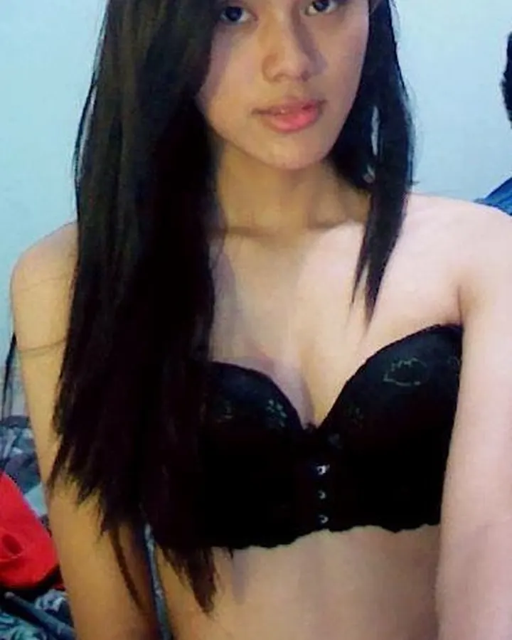 Femme trans asiatique aux cheveux noirs, en chemise sombre, regardant de côté dans un éclairage tamisé.